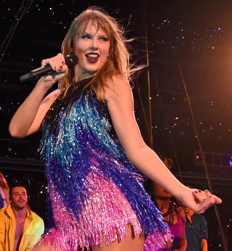 Taylor Swift performing in a dress with pink, purple, and blue glitter fringe